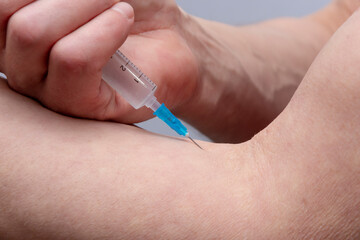 An elderly muscular man gives himself an injection into a vein on his arm, close-up. Perhaps he is...