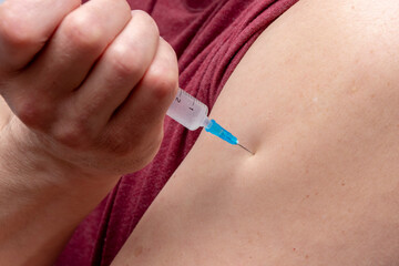 An elderly muscular man gives himself an injection in the shoulder, close-up. Perhaps he is injecting painkillers, has diabetes.