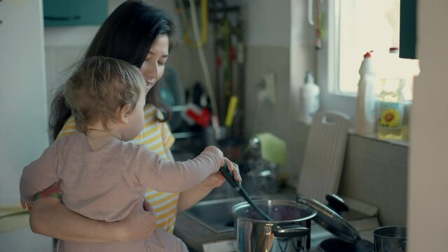 Cinematic authentic shot of happy mother and her little toddler baby boy son are having fun to make dough with flour together for baking cookies or bread in kitchen at home.
