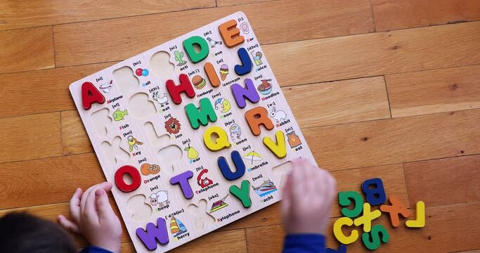Top view of a kid playing alphabet  puzzle and learning English on the floor.