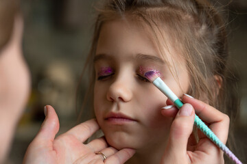 Naklejka premium mom uses a brush to apply shiny shadows on eyelids of her daughter