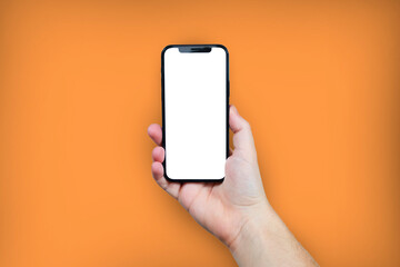 Fototapeta na wymiar Hand holding the black smartphone with blank screen and modern frame less design on orange colour background