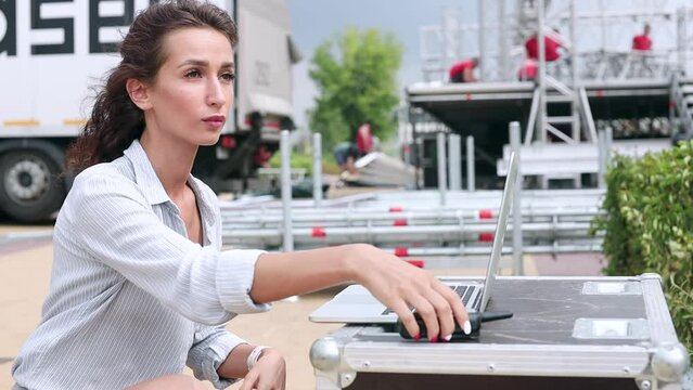 Installation of stage equipment and preparing for a live concert open air. Event manager portrait. Summer music city festival. Woman work with laptop.