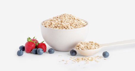 raw oat flakes in a light beige plate with a wooden spoon and strawberries and blueberries isolated on a white background