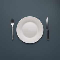 white empty plate with cutlery on dark gray background

