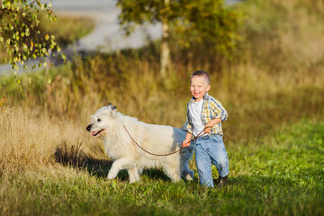 Happy smiling blond boy running with dog friend on farm