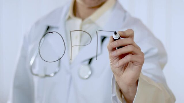 A young unrecognizable caucasian doctor in a white coat with a stethoscope writes the word open on the glass door of the hospital. Medicine, healthcare.