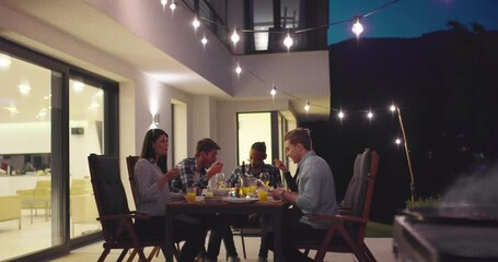 A group of friends enjoy while having dinner together in front of a luxury villa. A group of friends enjoy the barbecue and have fun in the late hours
