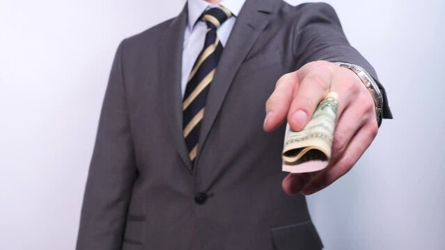 An unrecognizable businessman in a suit and tie takes out and shows several dollar bills from his pocket. Salary, payment for services or bribery, corruption.
