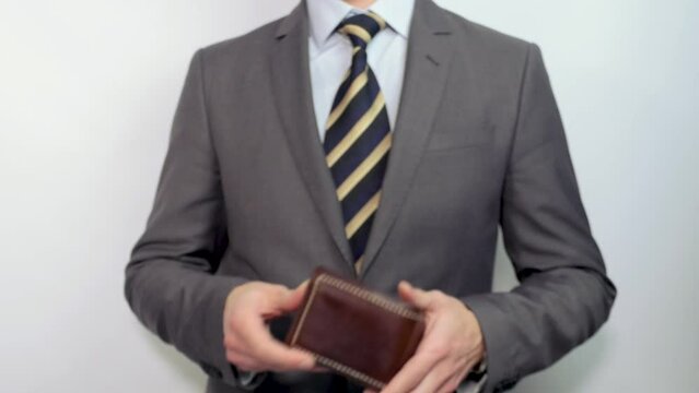 An unrecognizable businessman in a suit with a tie takes out and shows an empty leather wallet from his inside pocket. Crisis, lack of money, bankruptcy.