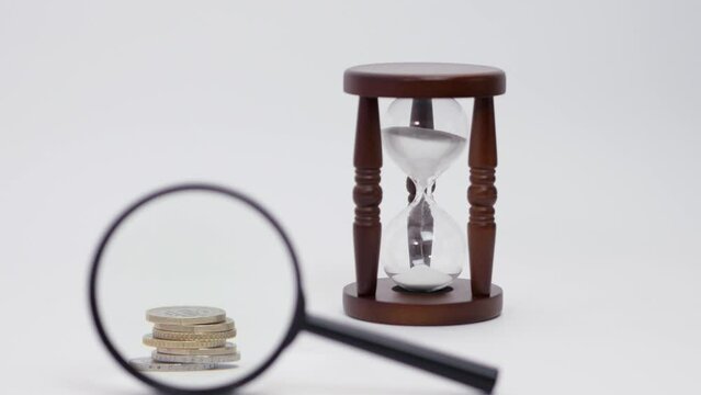 Magnifier focused on a stack of coins near the hourglass. The concept of time is money