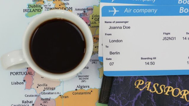 Male hand puts a cup of coffee on a map of Europe with a passport and plane tickets