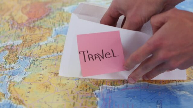 Male hand takes out money from the envelope with travel sticker note and puts dollar bills on the worls map