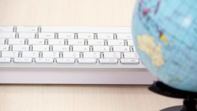 Spinning globe in front of white computer keyboard, concept of international business, distant office work