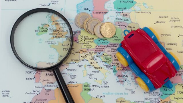 Black magnifying glass, euro coins and a toy car on the map of Europe, concept of car travel.