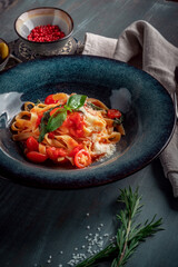 The classic tagliatelli pasta with tomato sauce is served on a blue plate. Italian dish with tomatoes, basil, parmesan and pasta