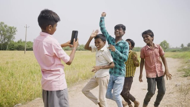 kid making video of his dancing friends for social media in the middle of road on mobile phone - concept of technology, village children and live streaming.