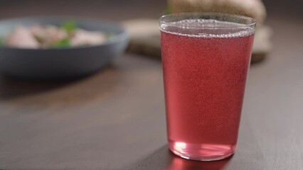 Slow motion pour pink drink in tumbler glass on wood table