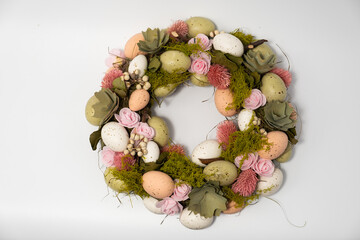 three blue spotted chicken eggs and a wreath of willow twigs on a white background, top view