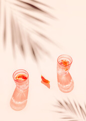Creative composition made of two glasse with cocktail or lemonade on beige pastel background with lobule of bloody orange. Summer refreshment concept. Sunlit flat lay. Minimal style. Top view
