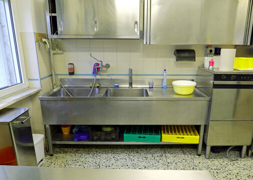 interior of an industrial kitchen with the large stainless steel sink and the dishwasher for washing pots and dishes