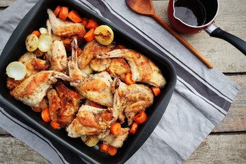 High Angle View of Roasted Rabbit Haunches in Pan with Stewed Vegetables on Rustic Wooden Table Surface