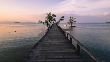 Fototapeta na wymiar Scenic view of long straight wooden pier over peaceful water in evening orange sky before sunset. Koh Mak Island, Trat Province, Thailand.