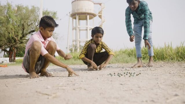 Indian village kids playing goli or marbles on near paddy field - concept of traditional game, summer holidays and leisure activities.