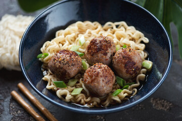 Close-up of a dark-blue bowl with ramen noodles and fried meatballs in miso broth, selective focus, studio shot