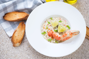 Crab risotto served in a white plate on a beige marble background, elevated view