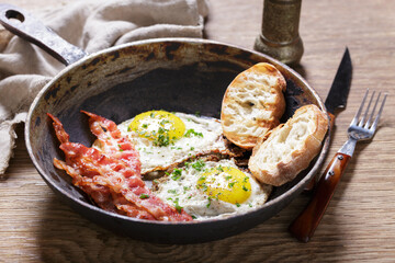 Breakfast with pan of fried eggs, bacon and toasts