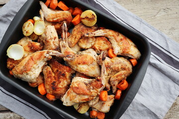 Roasted Rabbit Haunches in Pan with Stewed Vegetables on Rustic Wooden Table Surface