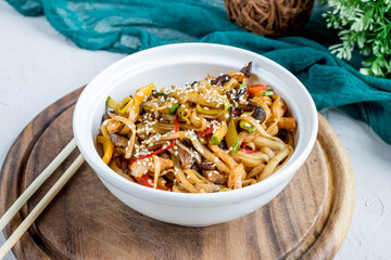 Udon noodles with chicken and vegetables on white bowl on wooden board