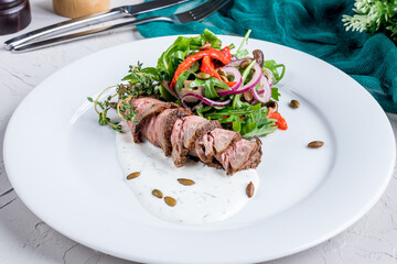 Salad with roast beef and fresh vegetables with sauce on a white plate