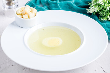 Chicken soup bouillon with egg and croutons on white bowl