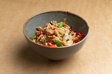 Noodles with chicken, bean pods and red pepper. On a brown background.