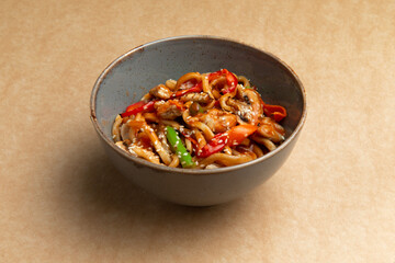 Noodles with chicken, bean pods and red pepper. On a brown background.