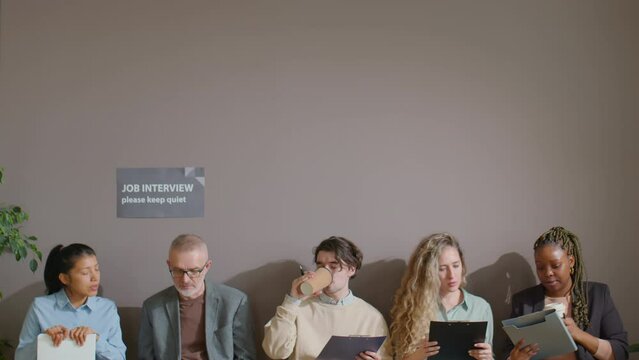 Multiethnic job candidates drinking coffee and discussing application forms while waiting in queue for interview in office
