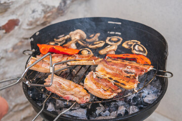 Black round metal barbecue with meat and vegetables already cooked on the grill. Round metal container for cooking barbecues with a grill placed on top full of fresh meat and mushrooms already cooked 