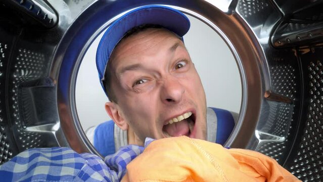 a home appliance repairman in blue uniform sticks his head into drum of washing machine and screams styroco from his mouth. He is dissatisfied and warns of danger. Repair of washing machines.