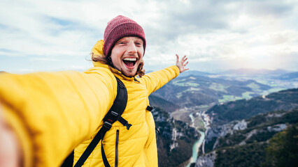 Young hiker man taking selfie portrait on the top of mountain - Happy guy smiling at camera -...