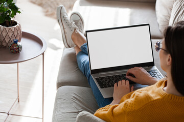 Young woman using laptop screen blank, mockup lying on sofa at home - obrazy, fototapety, plakaty