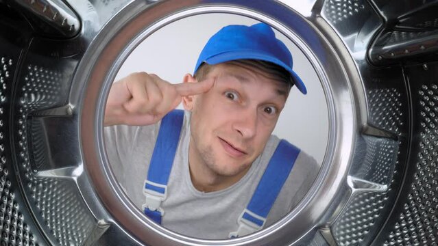 a home appliance repairman in blue uniform sticks his head into drum of washing machine and screams styroco from his mouth. He is dissatisfied and warns of danger. Repair of washing machines.