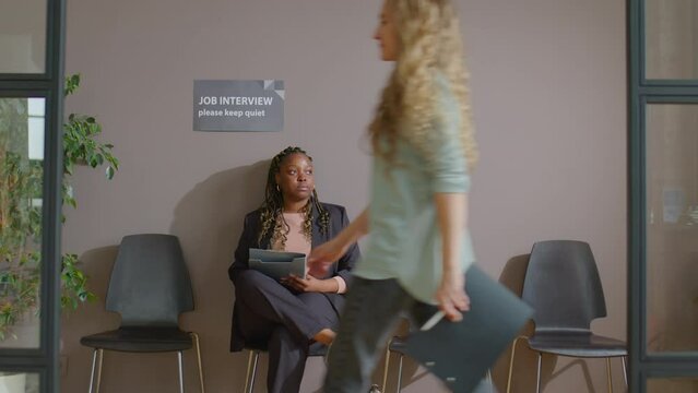 Zoom in shot of African American woman filling application form on clipboard while waiting for job interview in office as business people passing by her