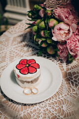 Stylishly decorated cake with a red flower pattern in a white plate with wedding rings on the table with a bouquet for the bride on the wedding day in the morning at breakfast