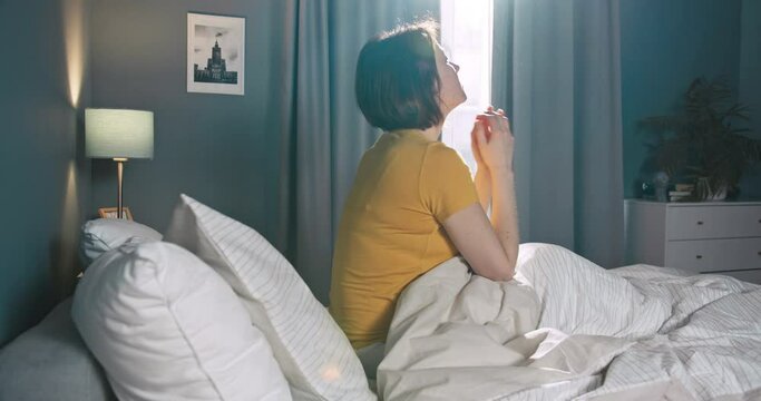 Depressed young caucasian woman sit alone in bed, feel stress and pounding fists. Beautiful caucasian female waking up in the morning after bad sleep.