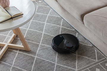 Robotic vacuum cleaner cleaning carpet at home next sofa - obrazy, fototapety, plakaty