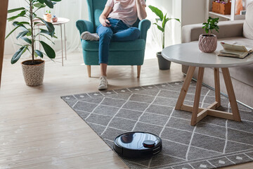 Robotic vacuum cleaner cleaning carpet, woman controls remote control and joy rest while sitting on...