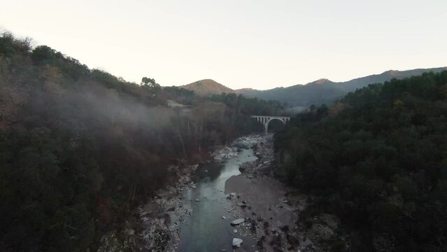 Rivi&egrave;re sauvage qui serpente jusqu'&agrave; un pont au milieu d'une vall&eacute;e dans la brume matinale de l'hiver dans les C&eacute;vennes du sud de la France.