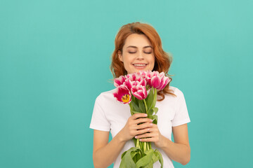 happy girl smelling tulip flower bouquet on blue background